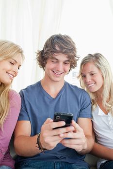 A man showing his friends what is on his phone as they sit on the couch 