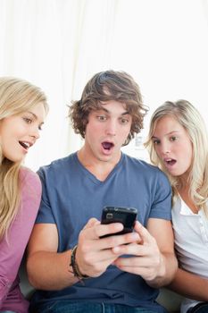 Friends sit on the couch looking shocked at what is on the phone 