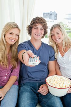 Three smiling friends with a bowl of popcorn and a tv remote looking at the camera 