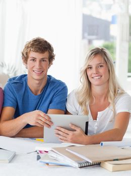 A couple smiling as they hold the tablet pc and look into the camera 