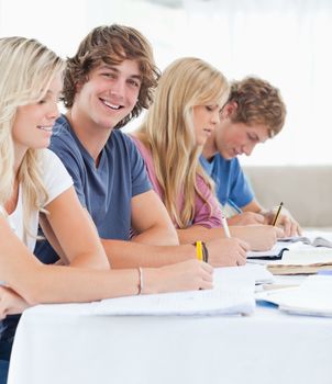 A close up shot of a smiling student sitting with his friends as he looks into the camera 