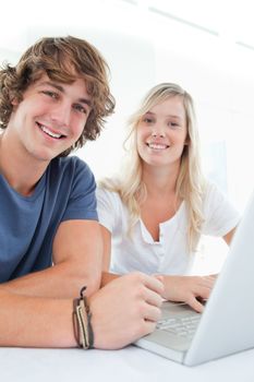 A close up of a smiling couple as they use a laptop while looking into the camera 