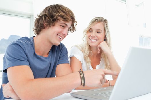A couple smile as they sot together as the man looks at the screen and the woman looks at him 