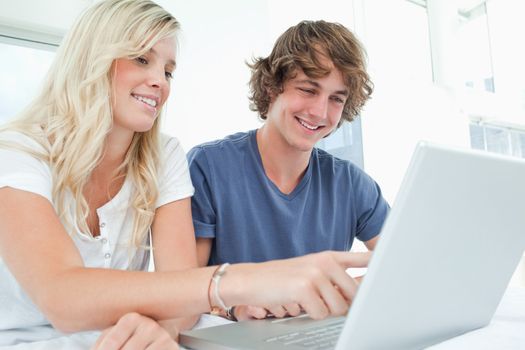 A couple sitting together using a laptop while the girl points at the screen 