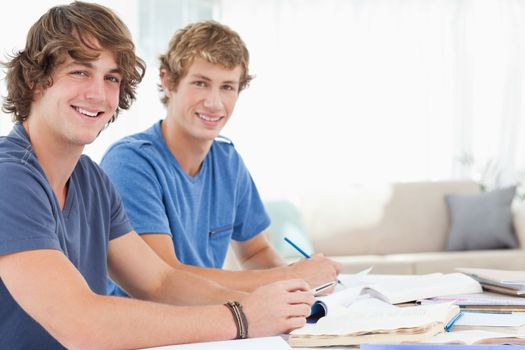 A pair of smiling students as they both look into the camera while they study 