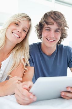 A smiling couple holding a tablet and looking at the camera while they sit together