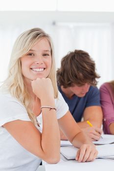 Close up of a smiling student with her friends as they all study while she looks into the camera 