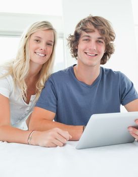 A close up of a smiling couple holding a tablet and looking at the camera