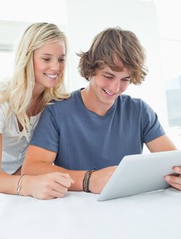 A smiling couple sit together and use a tablet 