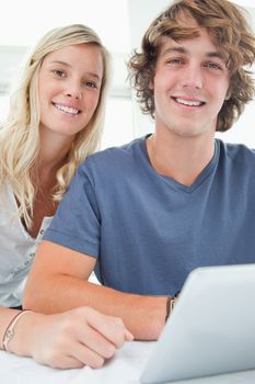 A close up of a smiling couple holding a tablet and looking at the camera