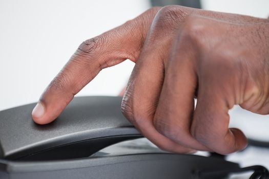 Close up of a masculine hand on a phone handset against a white background