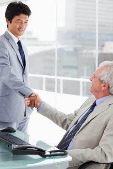 Portrait of a smiling employee shaking the hand of his manager in an office