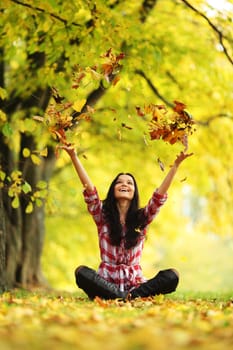 woman drop up leaves in autumn park