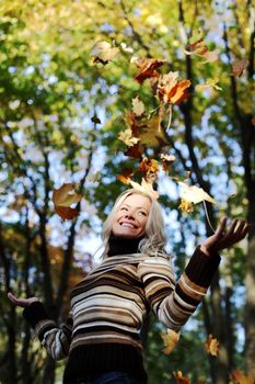 woman drop up leaves in autumn park