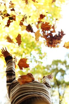 woman drop up leaves in autumn park