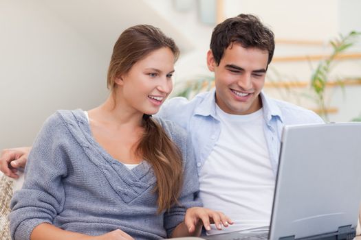 Delighted couple using a laptop in their living room