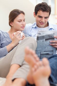 Couple reading a newspaper while lying on a sofa looking away from the camera