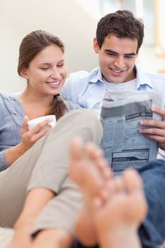 Couple reading a newspaper while lying on a couch looking away from the camera