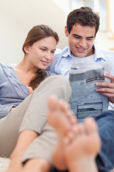 Portrait of a couple reading a newspaper while lying on a couch in their living room