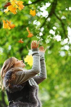 woman drop up leaves in autumn park