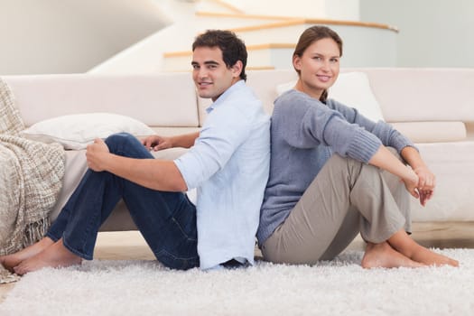 Young couple sitting back to back in their living room