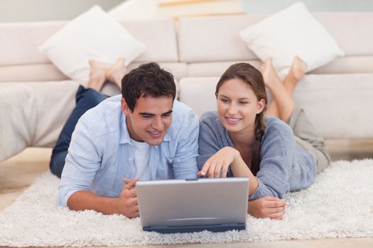 Couple looking for something on the internet while lying on a carpet