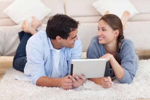 Cute couple using a tablet computer while lying on a carpet
