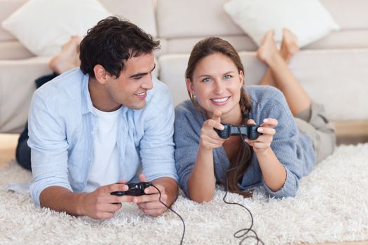 Lovely couple playing video games while lying on a carpet