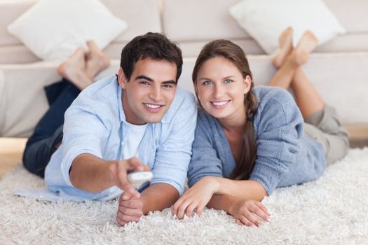 Smiling couple watching TV while lying on a carpet in their living room