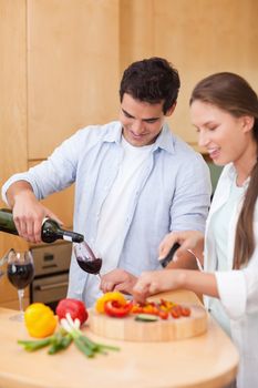 Portrait of a cute man pouring a glass of wine while his wife is cooking in their kitchen