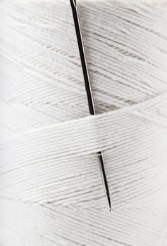 Macro view of reel of white thread with needle