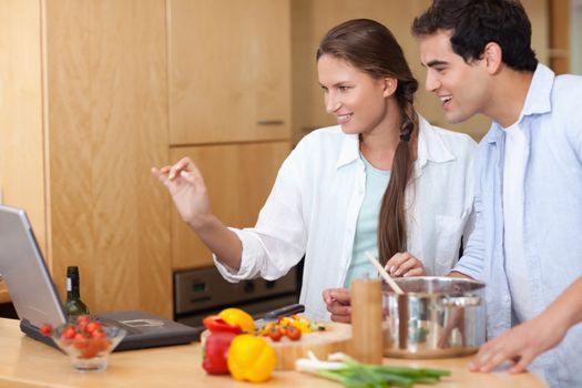Smiling couple using a laptop to cook in their kitchen