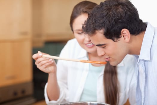 Close up of a man trying his wife's sauce in their kitchen