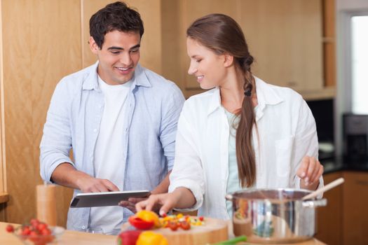 Charming couple using a tablet computer to cook in their kitchen