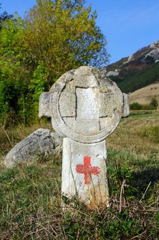 old stone cross with touristic sign on a hiking trail witch crosses an abandoned cemetery near Rimetea, Romania