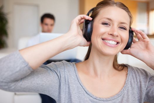 Smiling woman with headphones on with man sitting behind her on the sofa