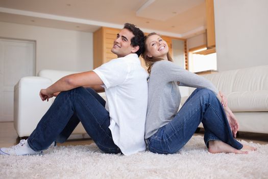 Side view of young couple sitting on the carpet back-to-back