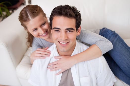 Smiling man getting hugged by his girlfriend on the sofa