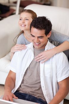 Young woman hugging her boyfriend that is working on the laptop