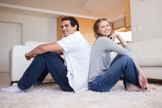 Side view of smiling young couple sitting on the floor back-to-back