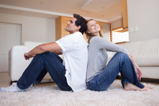 Side view of young couple sitting on the floor back-to-back