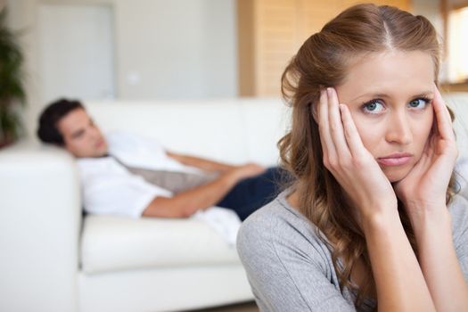 Young woman suffering from headache with man on the sofa behind her