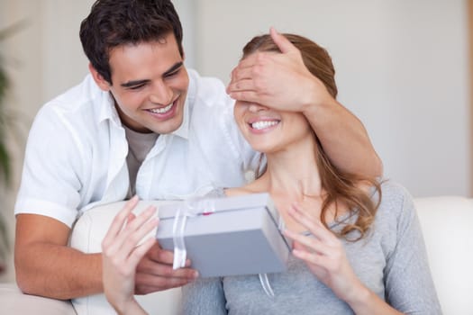 Young man covering the eyes of his girlfriend while giving her a present