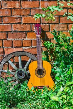 Guitar and the old wagon wheel against a brick wall