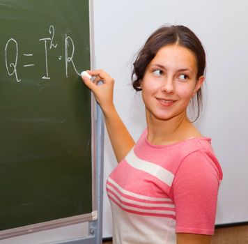 Beautiful girl in a physics class writes the formula on the blackboard