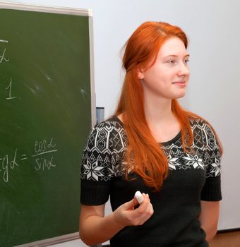 Beautiful red-haired girl in math class writing formulas on a blackboard