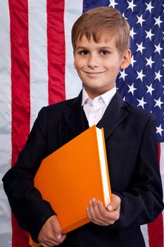 �ute schoolboy is holding an orange book against USA flag