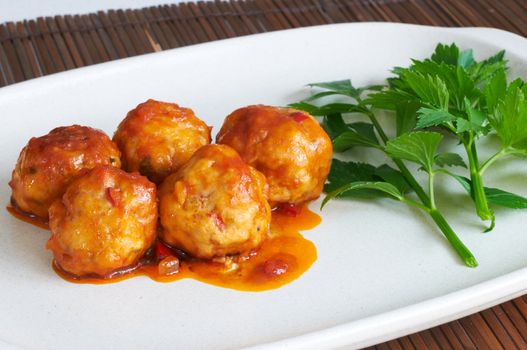 Meat balls in tomato sauce on a white dish with some parsley leaves