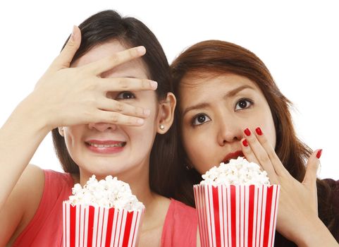 Two young women eating popcorn while watching a scary movie (on white background)