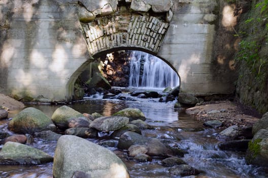 Retro architecture arch in wall and stream flowing from waterfall.